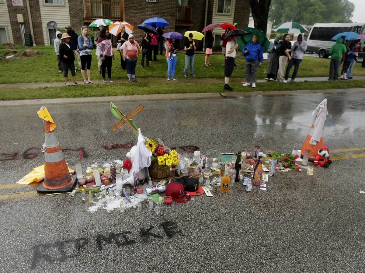 People gather next to a makeshift memorial for Michael Brown on Saturday located at the site where Brown was shot by police a week ago in Ferguson, Mo. Brown's shooting in the middle of a street following a suspected robbery of a box of cigars from a nearby market has sparked a week of protests, riots and looting in the St.