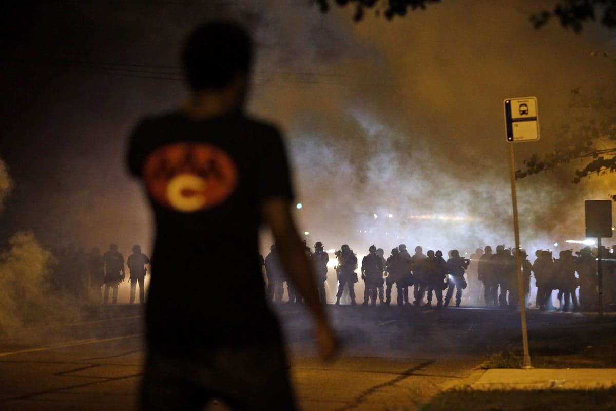 A man watches as police walk through a cloud of smoke during a clash with protesters Wednesday in Ferguson, Mo.