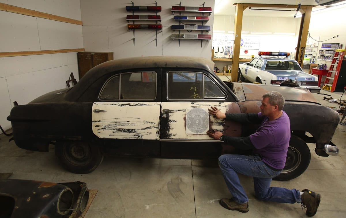 Seattle police Officer Jim Ritter of the Seattle Metropolitan Police Museum holds an original side-door decal that is being used in the restoration of a 1949 Washington State Patrol car.