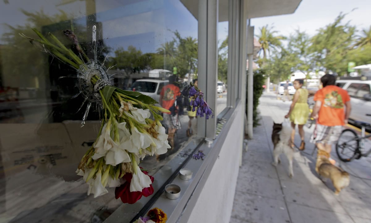 Flowers are placed through a bullet hole on a window of IV Deli Mart, where part of Friday night's mass shooting took place.