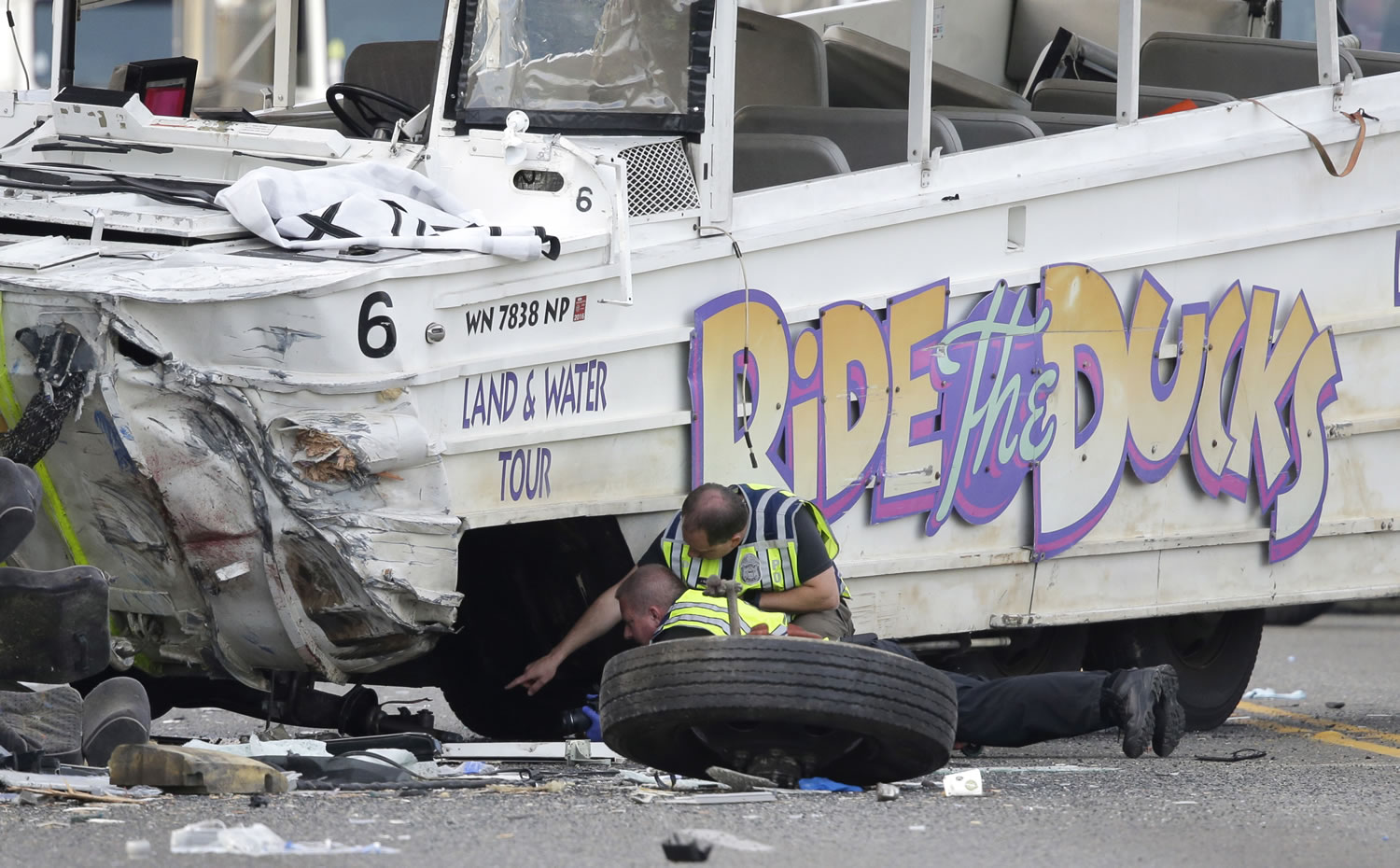 Seattle Police officers look under a &quot;Ride the Ducks&quot; tourist vehicle as a tire and wheel from the bus sits nearby before the bus is loaded onto a flatbed tow truck Thursday, Sept. 24, 2015, after it was involved in a fatal crash with a charter passenger bus earlier in the day in Seattle. (AP Photo/Ted S.