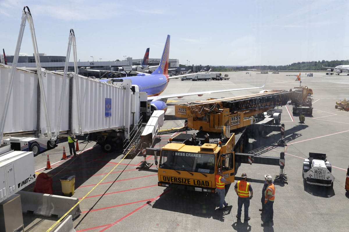 A large crane stands ready to lift a jetway, right, that had a mechanical failure and slowly lowered to the ground Tuesday while connected to a Southwest Airlines airplane at Seattle-Tacoma International Airport.