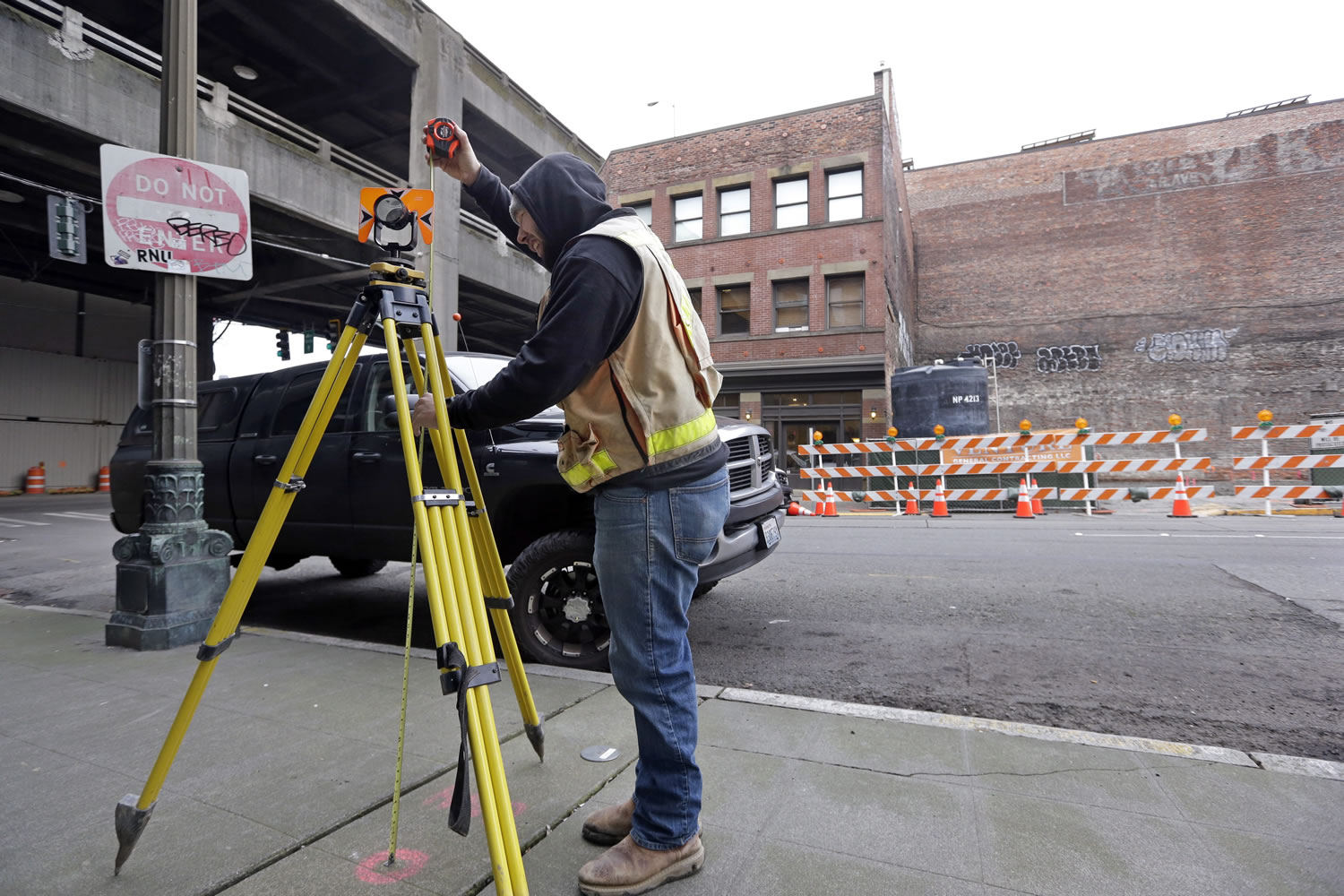 Surveyor Zach Cloe measures at a benchmark for settling of the buildings behind him and next to the Alaskan Way Viaduct, upper left, last week in Seattle.