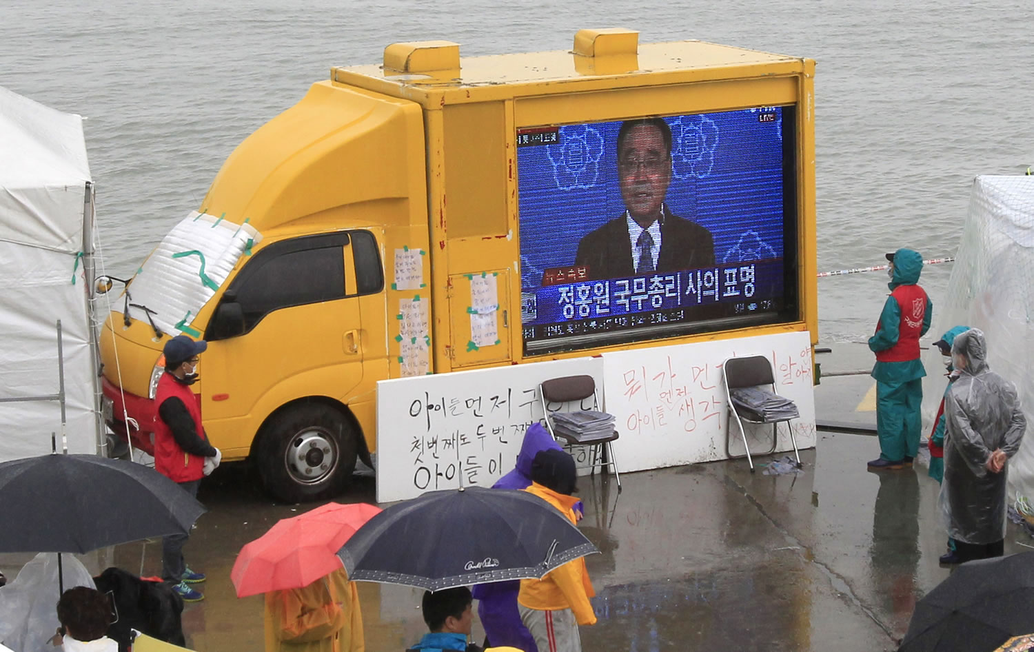 Relatives of passengers aboard the sunken ferry Sewol and onlookers watch a television news program Sunday showing South Korean Prime Minister Chung Hong-won offering his resignation at a port in Jindo, South Korea.