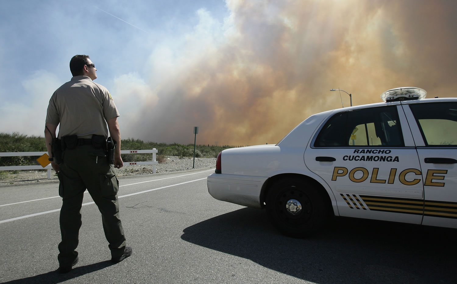 A San Bernardino Sheriff's deputy keeps an eye on a brush fire burning Wednesday near Rancho Cucamonga, Calif.