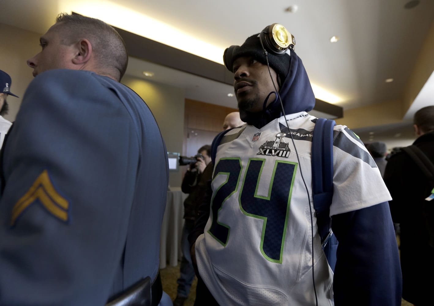 A member of the New Jersey state police escorts Seattle Seahawks running back Marshawn Lynch, right, through an area where a media availability was being held at the team's hotel Wednesday, Jan. 29, 2014, in Jersey City, N.J. The Seahawks and the Denver Broncos are scheduled to play in the Super Bowl XLVIII football game Sunday, Feb. 2, 2014.