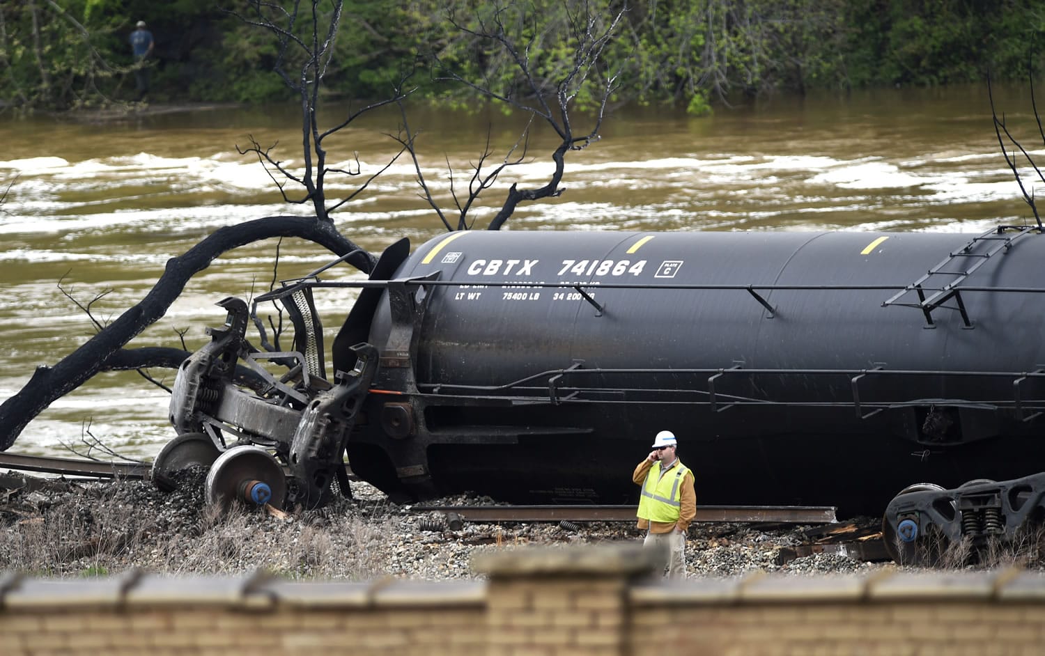 A worker stands by a damaged tanker car where several CSX tanker cars carrying crude oil derailed and caught fire along the James River near downtown Lynchburg, Va., Thursday.