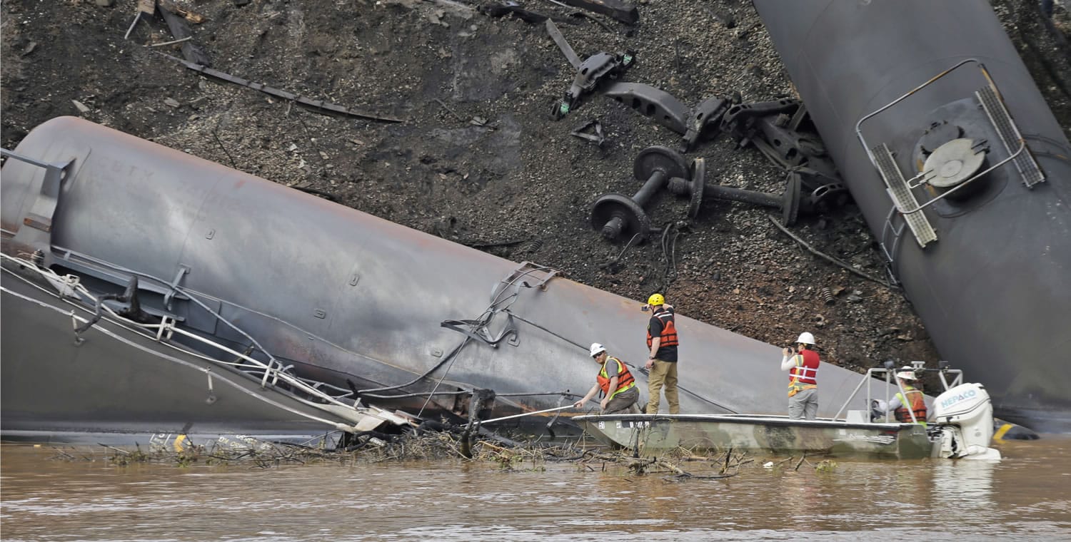 Survey crews in boats look over tanker cars as workers remove damaged tanker cars along the tracks where several CSX tanker cars carrying crude oil derailed and caught fire along the James River near downtown Lynchburg, Va., Thursday, May 1, 2014.  Virginia state officials were still trying Thursday to determine the environmental impact of the train derailment.