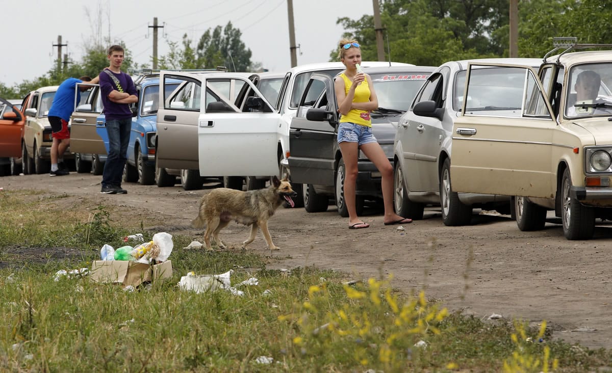 People stand at their cars while waiting in line to leave Ukraine at the Ukrainian-Russian border checkpoint Thursday in Izvaryne, eastern Ukraine.