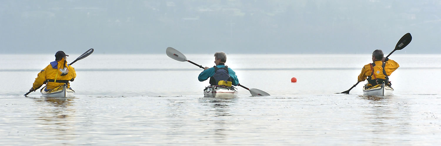 Kayakers paddle across a calm Vancouver Lake.