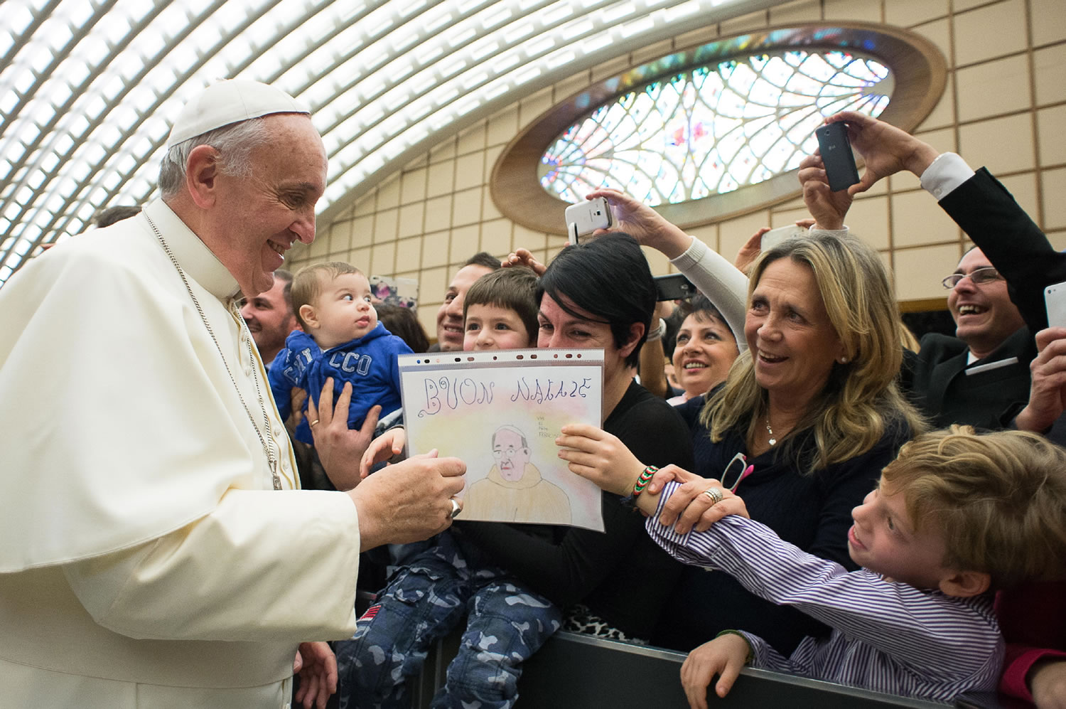 In this picture made available by the Vatican newspaper L' Osservatore Romano, Pope Francis is presented by a child with a drawing depicting a Pope's portrait and a writing which reads Merry Christmas, during an audience with the Holy See's employees in the Paul VI hall at the Vatican, Monday, Dec. 22, 2014.