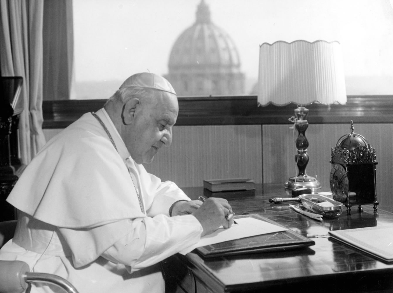 Pope John XXIII sits at his working desk on April 15, 1962, in his studio in a tower in the Vatican gardens. In the background is the dome of St.