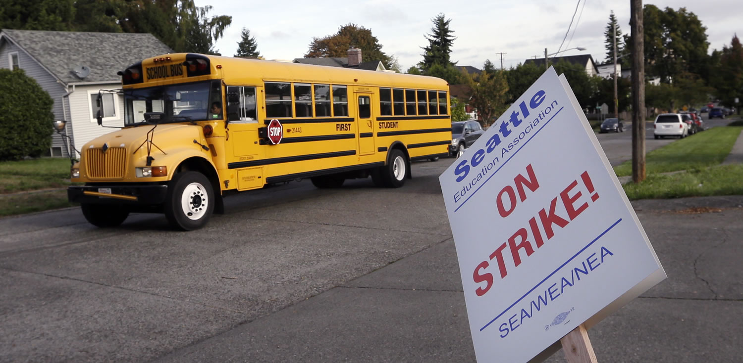 A school bus for a private school drives past a striking teacher in front of West Seattle Elementary School on Wednesday in Seattle. Teachers in Seattle began walking picket lines after last-minute negotiations over wages and other issues failed to avert a strike in Washington state's largest school district. Classes for 53,000 Seattle Public Schools students were canceled Wednesday, on the scheduled first day of school.
