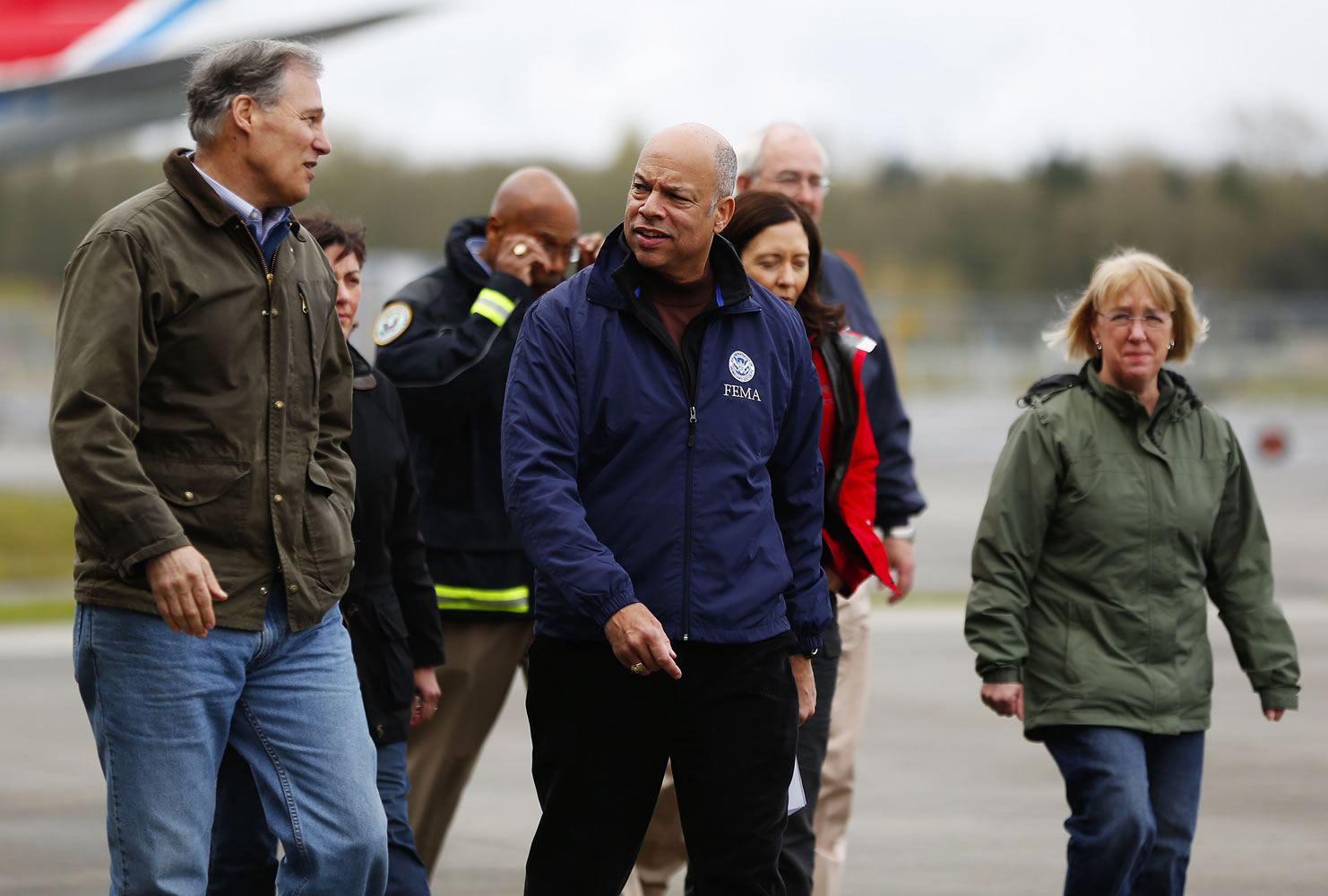 Gov. Jay Inslee, left, speaks with Secretary of Homeland Security Jeh Johnson, center, at Paine Field as they walk to the podium Sunday with officials including Sens. Maria Cantwell, in red, and Patty Murray, in green.