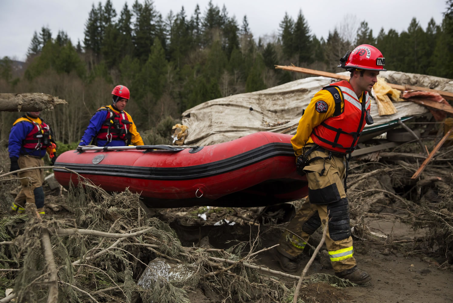 Rescue workers carry an inflatable boat to the flooded area in the debris field caused by the massive mudslide above the North Fork of the Stillaguamish River onto Highway 530, as recovery efforts continue, near Oso on Tuesday.