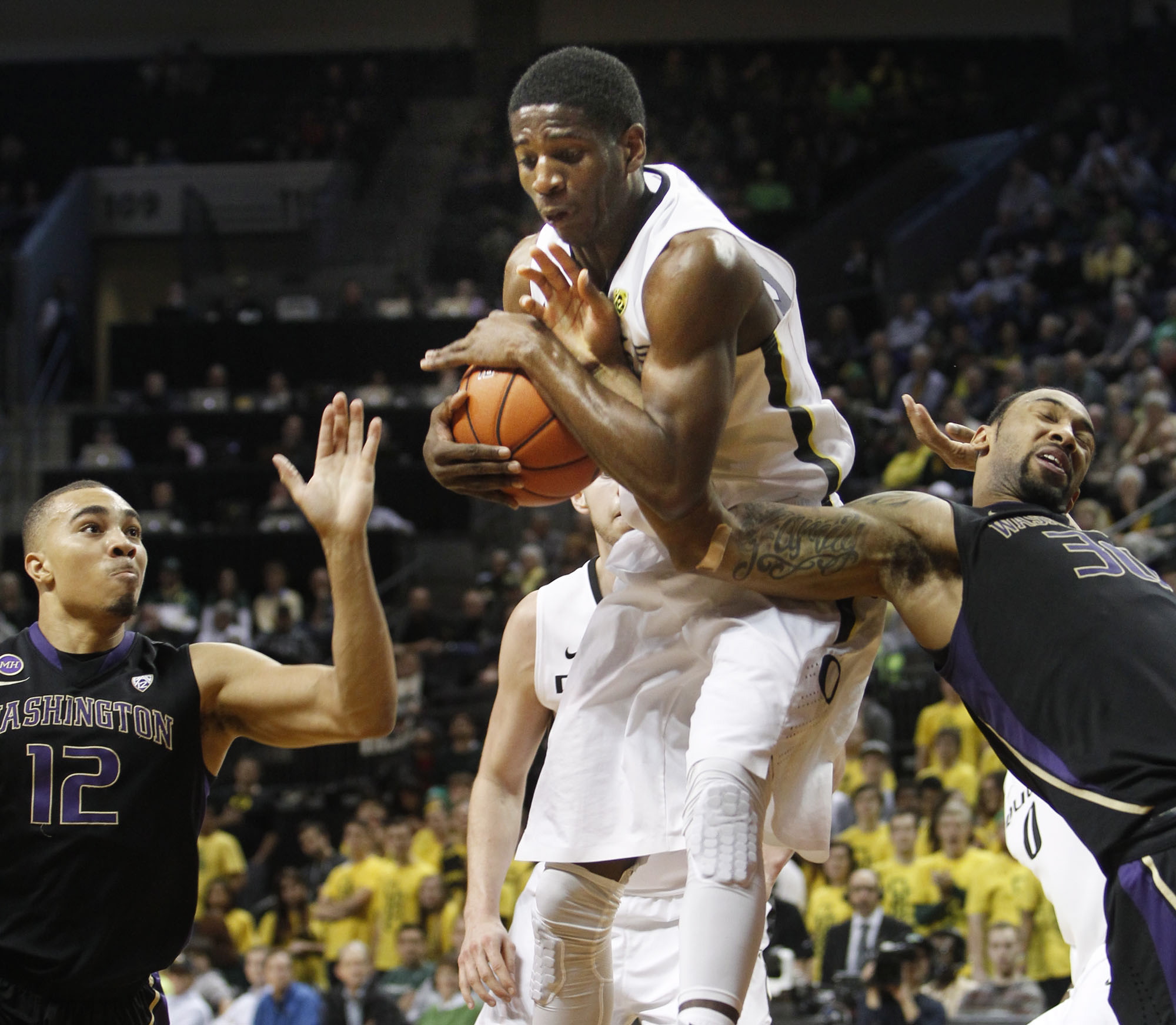Oregon's Damyean Dotson, center, comes down with a rebound against Washington's Andrew Andrews, left, and Desmond Simmons during the second half an NCAA college basketball game in Eugene, Ore., on Wednesday, Feb. 19, 2014. Oregon won 78-71.