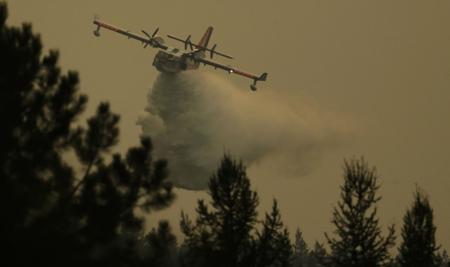 An airplane flies through smoky air as it drops water on a wildfire that flared up in the late afternoon near Omak, Wash., Thursday, Aug. 27, 2015. (AP Photo/Ted S.