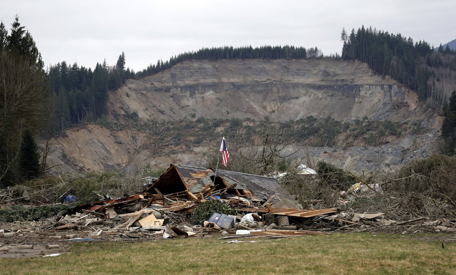 Associated Press files
A flag stands March 25 in the ruins of a home left at the end of the deadly mudslide in Oso. A new report outlines safety improvements based on lessons learned from the slide.