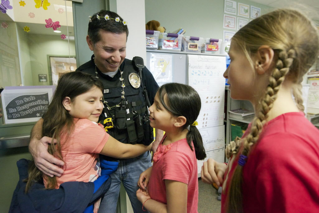Vancouver Police Detective Adam Millard receives a goodbye hug from third grade students Berenice Pintor, 9, left, and Maritza Sanchez, 9, after being presented with flowers as a gift from Katya Oleynick, 9, right, at Fruit Valley Elementary School in April.