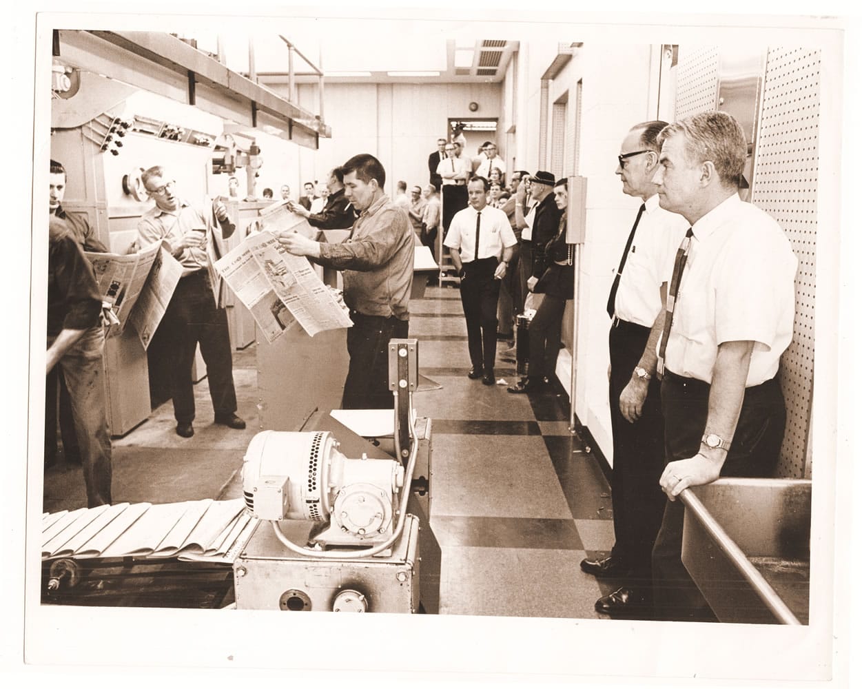 With pressmen and a crowd, Don Campbell, Morrie Shore and Jack Campbell watch the first run on the new Goss Metro Press.