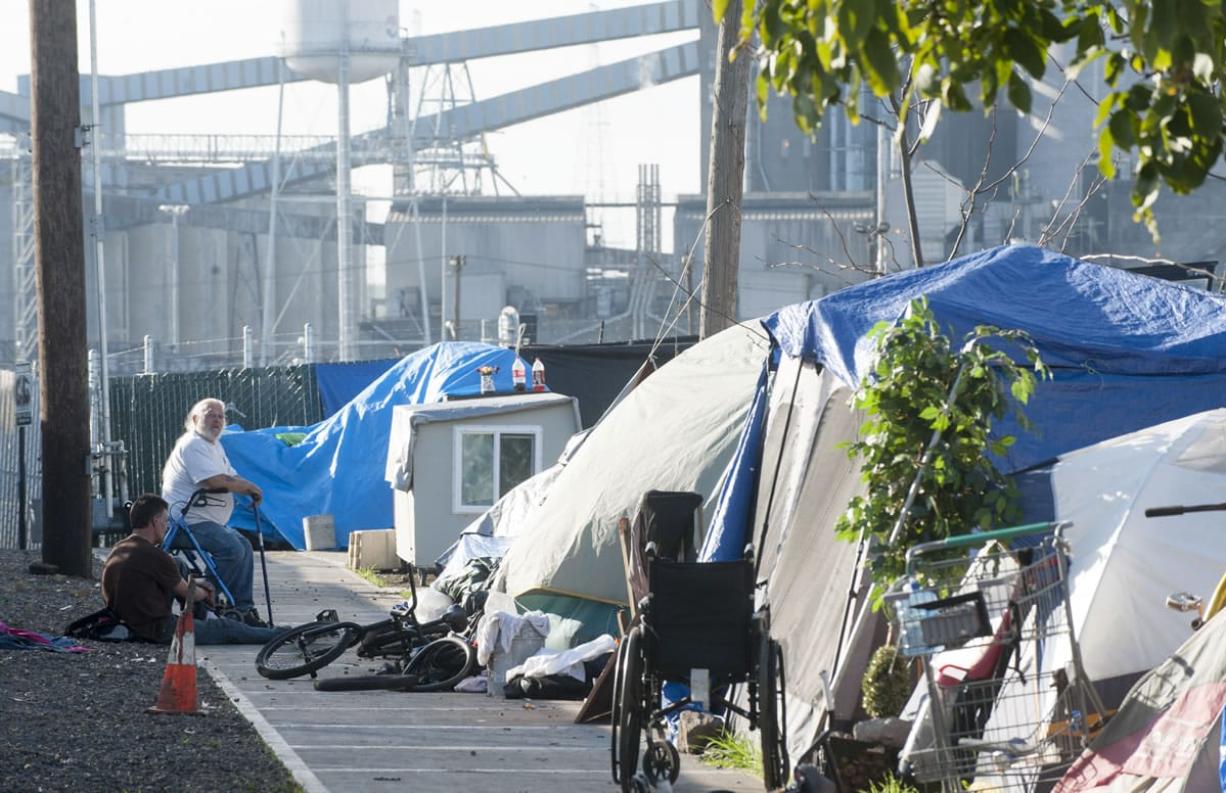 Residents sit at a homeless encampment in Vancouver earlier this month. Last weekend, a group of gun-toting volunteers patrolled the camp at night to provide security to the homeless living there. The group intends to return this weekend.