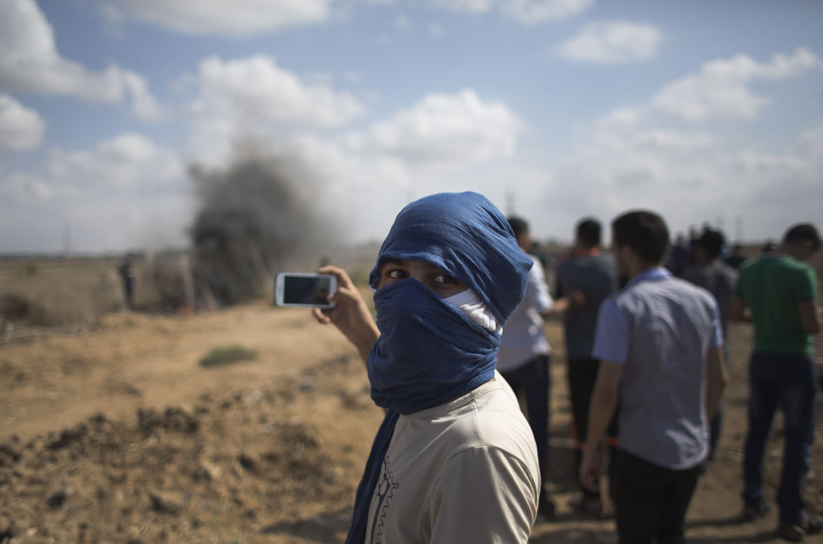 A Palestinian protester films with his cellphone Friday during clashes with Israeli soldiers on the Israeli border at Eastern Gaza City.