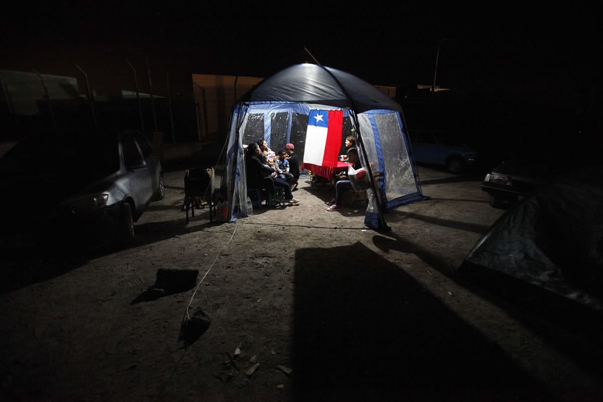 People take shelter under a tent decorated with a Chilean flag after evacuating their homes due to earthquakes Thursday in Alto Hospicio, Chile.