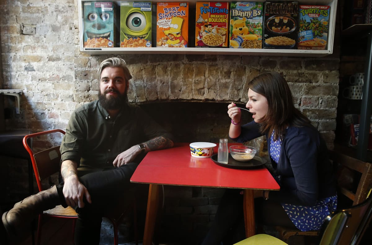 Alan Keery, one of the twin brothers who developed and own the Cereal Killer Cafe in  Brick Lane, London, talks to the Associated Press at the cafe, as customer Melanie Wolstenholme eats a late afternoon bowl of cereal Wednesday.
