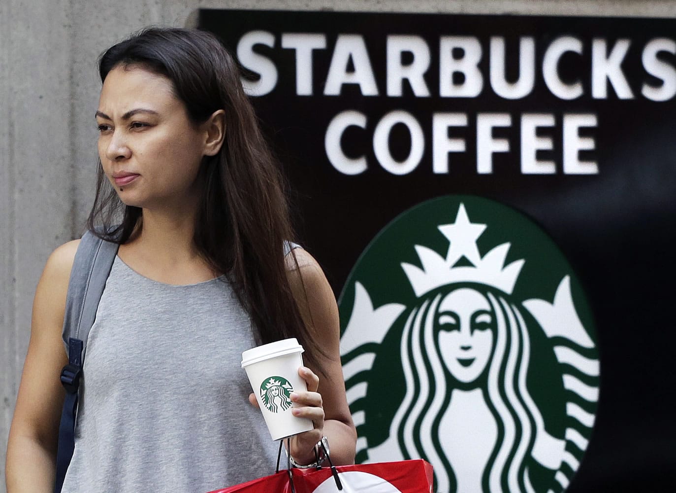 In this July 16, 2015, photo, a woman walks out of a Starbucks with a beverage in hand, in New York. Starbucks reports quarterly earnings on Thursday, Oct. 29, 2015.