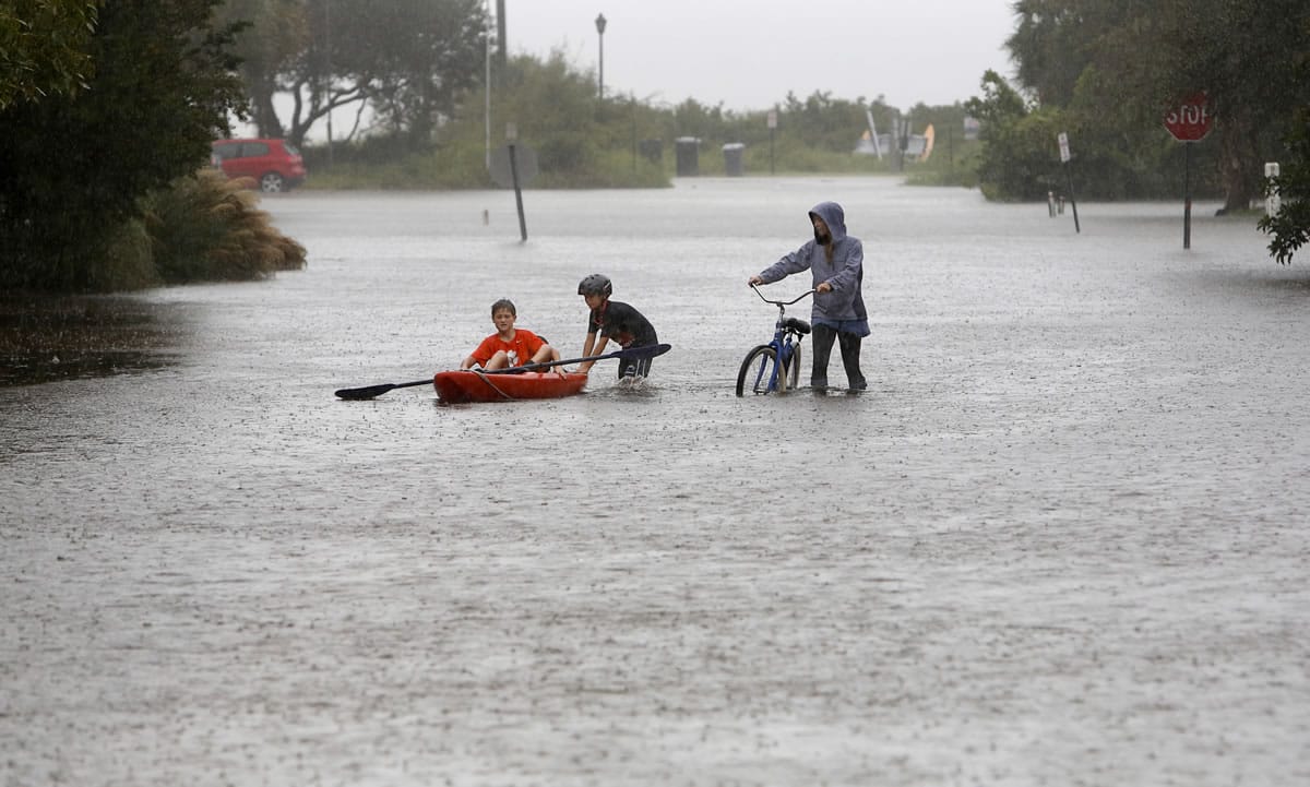 Joey Virgilio, 11, at far left, sits in a kayak while his brother, Will, 9, wades in the water as mom, Kristen, pushes a bike down Station 30 during flood waters on Sullivan&#039;s Island Saturday. Rain pummeling parts of the East Coast showed little sign of slackening Saturday, with record-setting precipitation prolonging the soppy misery that has been eased only by news that powerful Hurricane Joaquin will not hit the U.S.