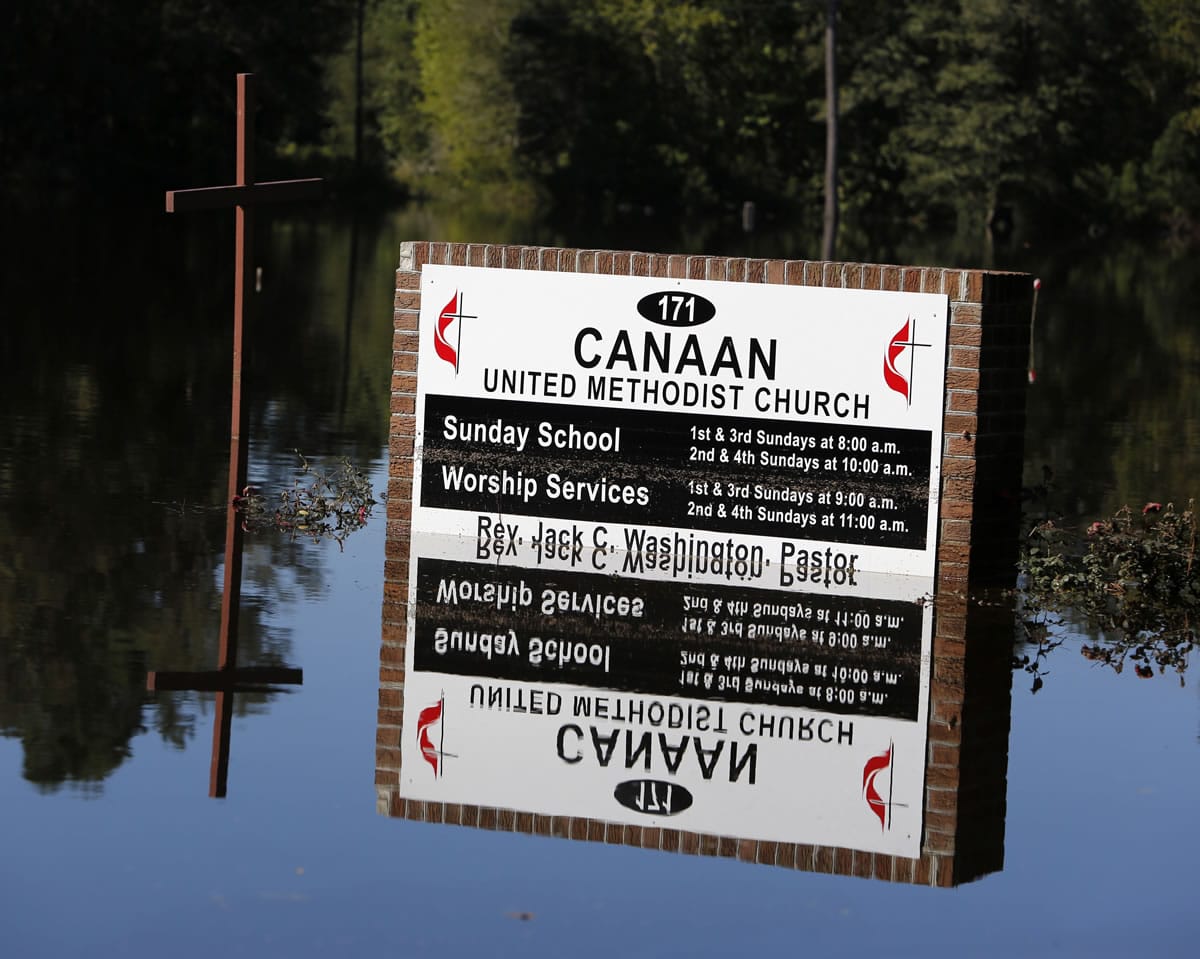 The church sign and cross are reflect in the floodwaters at Canaan United Methodist Church near Summerville, S.C., on Thursday. The church had a couple caskets come out of the ground at their cemetery beside the church during the flooding this week.