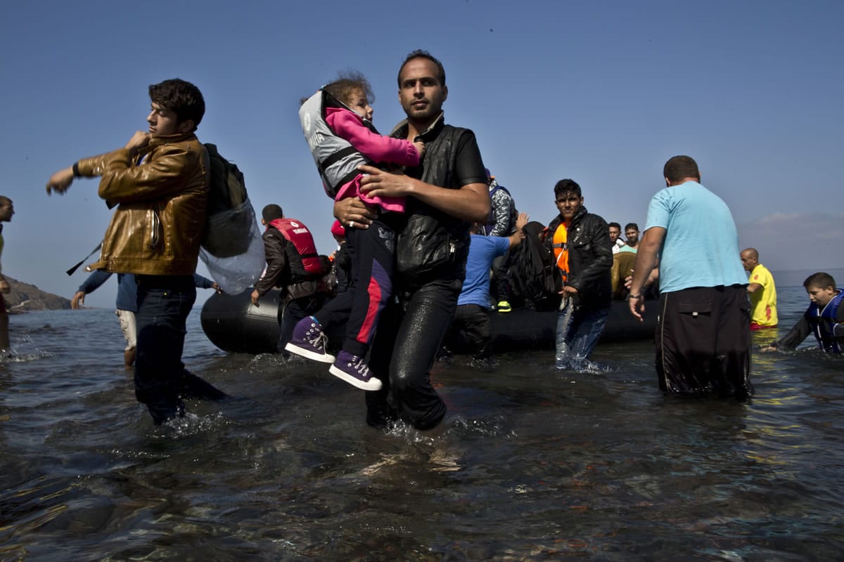 A Syrian refugee man carrying his daughter rushes to the beach Sunday as he arrives on a dinghy from the Turkish coast to the northeastern Greek island of Lesbos.