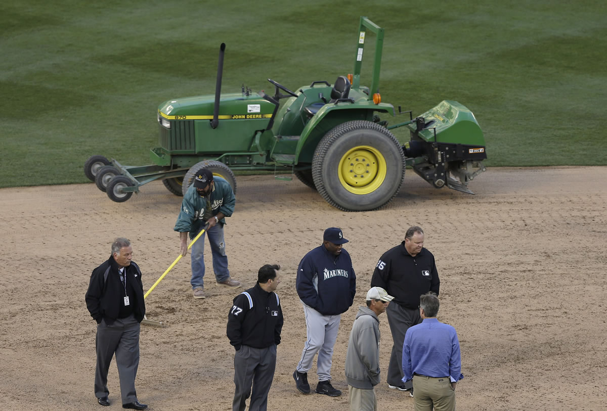 Seattle Mariners manager Lloyd McClendon, bottom center, talks with umpires Jim Reynolds (77) and Fieldin Culbreth (25) as members of the grounds crew work on the infield before a baseball game between the Mariners and the Oakland Athletics was postponed for unplayable field conditions.