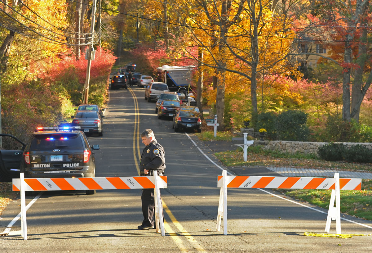 An officer stands at a blocked road Friday as police search the area around a home in Weston, Conn. Human remains were found.