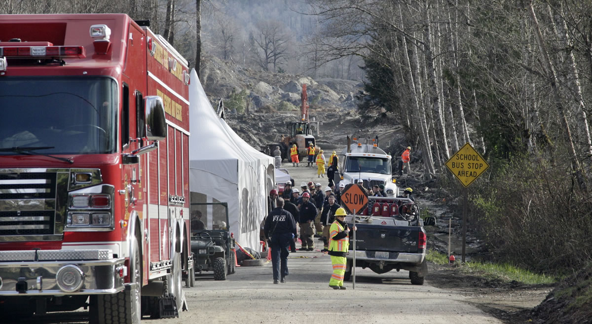 Emergency personnel stage on Highway 530 as work to clear debris from the roadway left behind from a deadly mudslide continues behind, Wednesday, April 2, 2014, in Oso, Wash. Officials have so far confirmed the deaths of 29 people, although only 22 have been officially identified in information released Wednesday morning by the Snohomish County medical examiner's office.