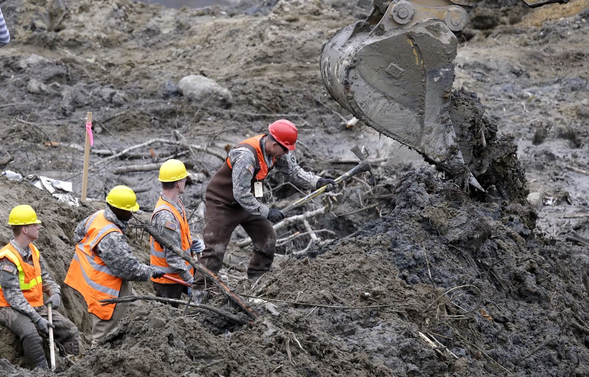 Workers use hand tools next to heavy equipment at the scene of a deadly mudslide nearly two weeks earlier nearby Thursday in Oso.