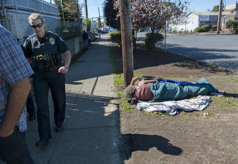 Commander Amy Foster, left, joins elected officials and others on Sept. 21 as they tour an area of downtown Vancouver facing issues with homelessness as a man sleeps on the ground nearby.