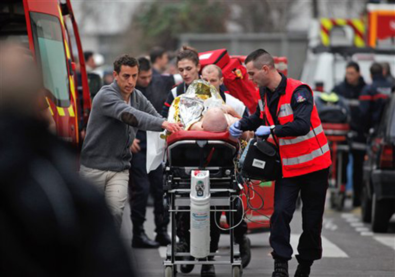 An injured person is transported to an ambulance after a shooting, at the French satirical newspaper Charlie Hebdo's office, in Paris, Wednesday, Jan. 7, 2015. Masked gunmen stormed the offices of a French satirical newspaper Wednesday, killing at least 11 people before escaping, police and a witness said. The weekly has previously drawn condemnation from Muslims.