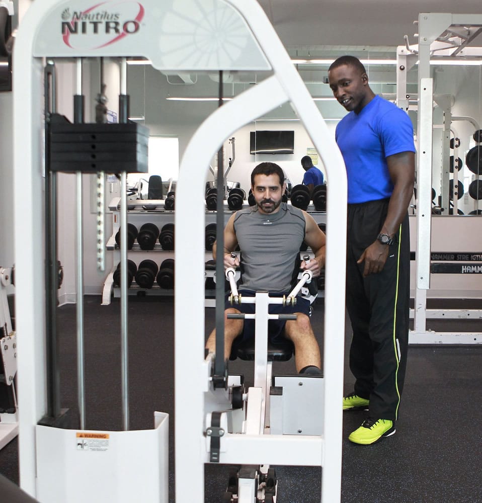 Fitness instructor Jeff Pierre watches over as Eddie Alvarez performs a rowing workout in the Miami Herald's on-site fitness center.