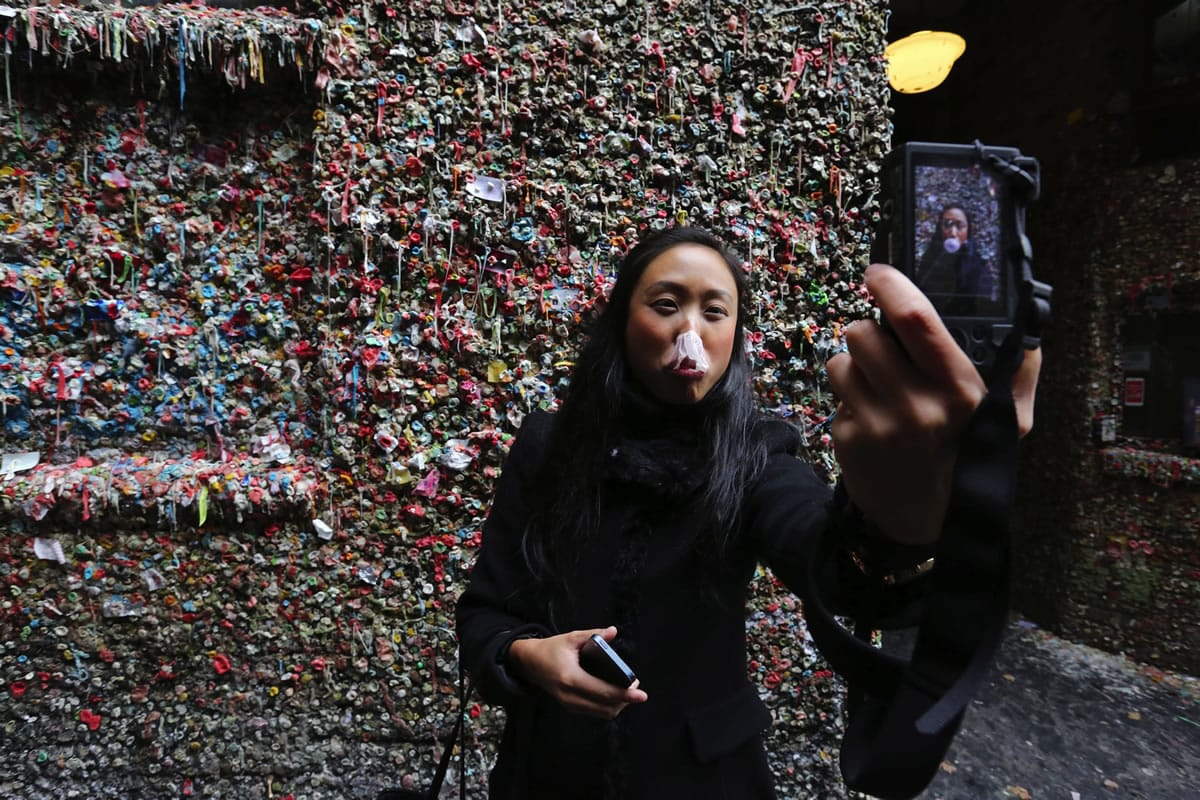Silvia Lim&#039;s gum bubble bursts as she records with her phone. Visiting from Sweden, she takes a selfie at the gum wall attraction in Seattle&#039;s Post Alley. The gum wall will be scrubbed clean beginning today for the first time in its existence.