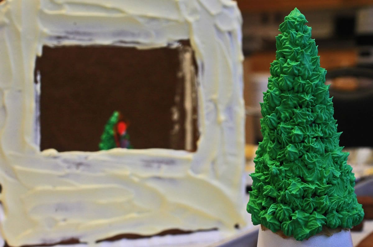 A Christmas tree made from royal icing waits to be placed on a gingerbread house.