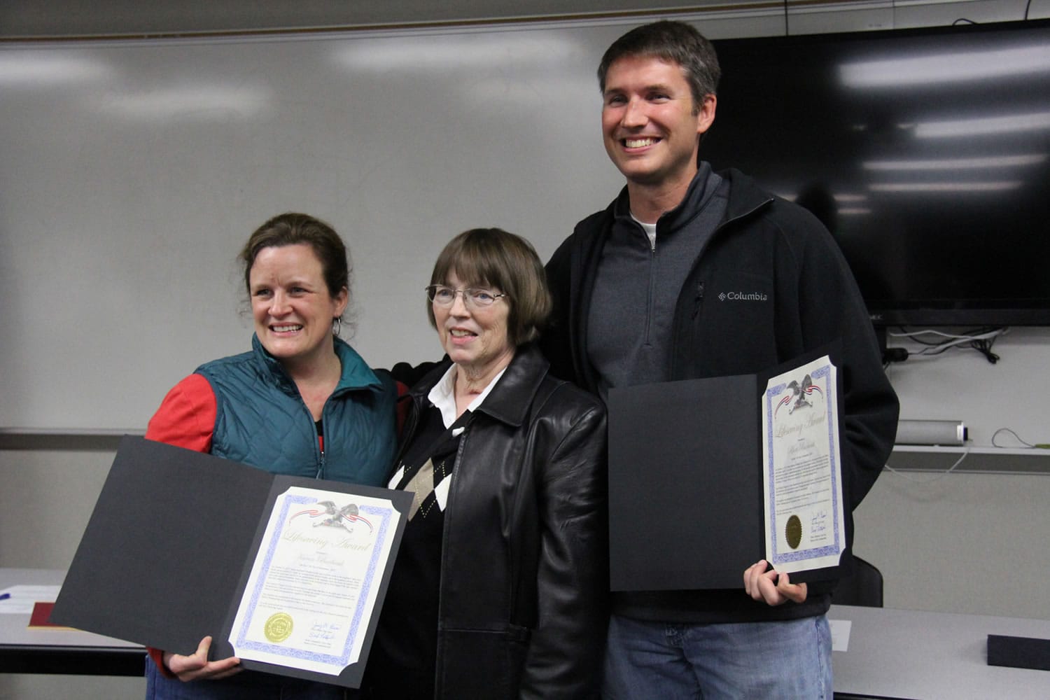 Karen Burbank, 39, left, and husband Rhett, 40, hold the lifesaving awards they were presented Tuesday for coming to the aid of their neighbor Sharon Miller, 65, center.