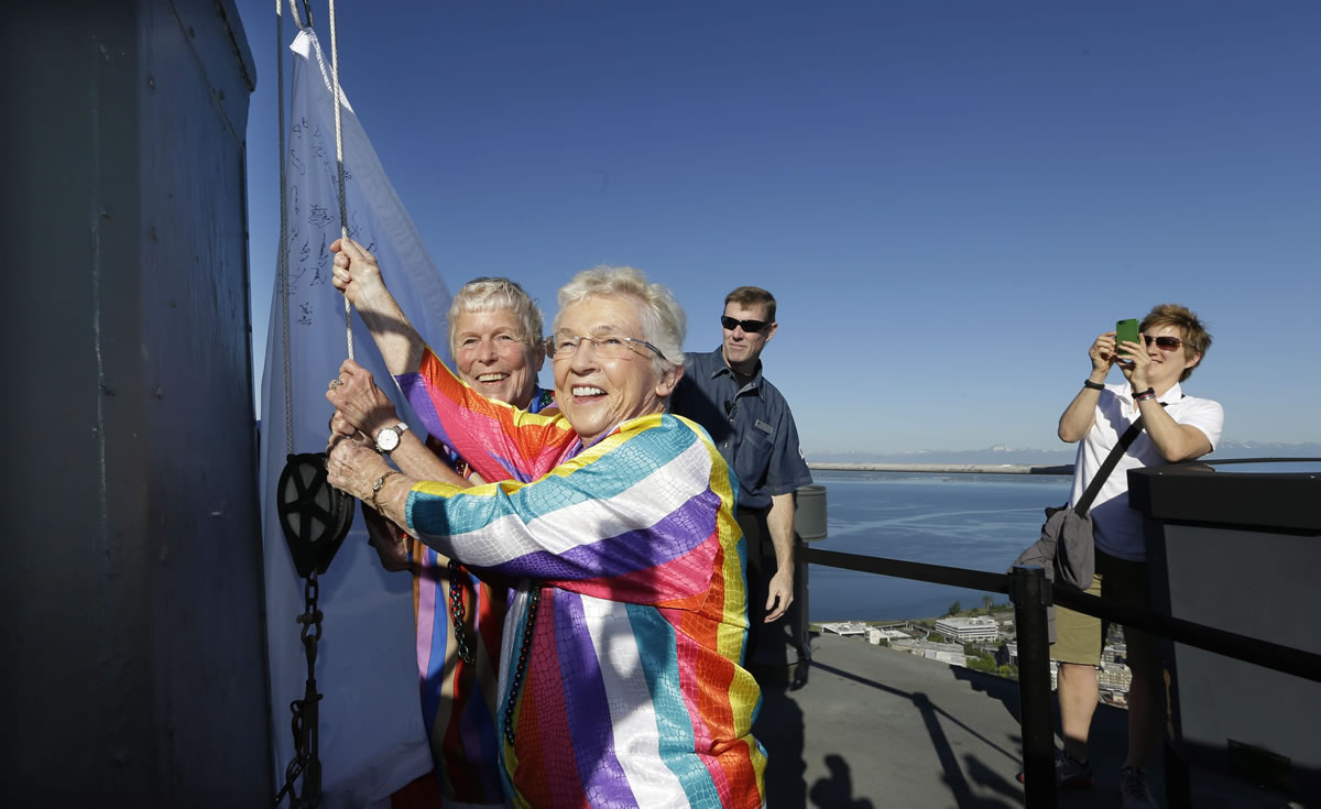 Associated Press files
Jane Abbott Lighty, left, and wife Pete-e Petersen raise a giant marriage equality flag in June atop the Space Needle in Seattle.