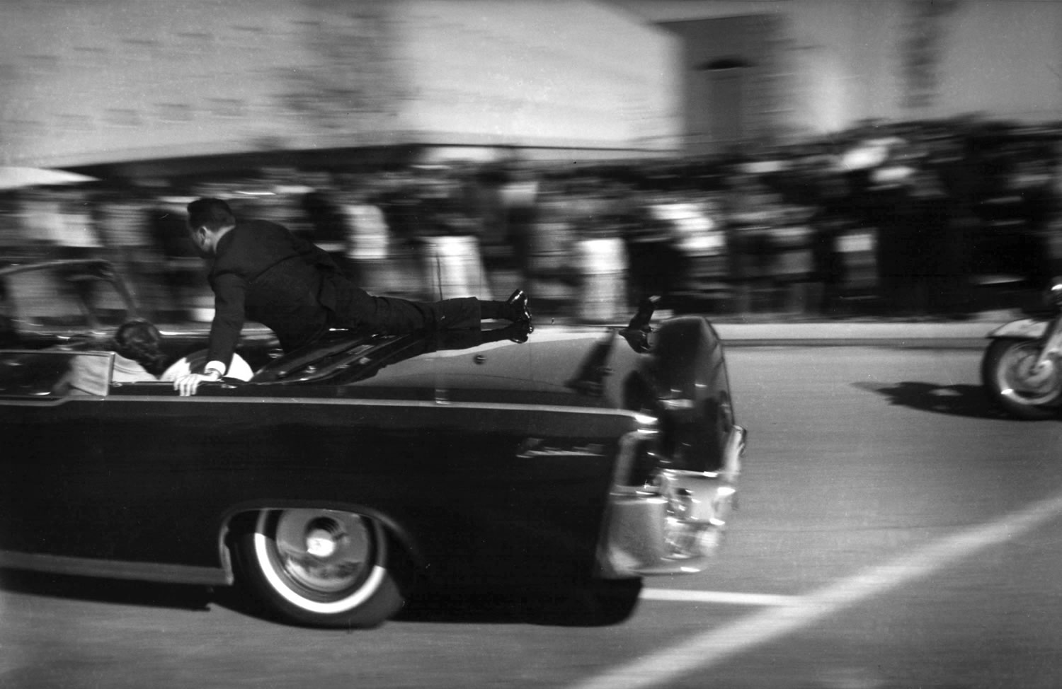The limousine carrying President John F. Kennedy races toward the hospital seconds after he was shot in Dallas on Nov. 22, 1963. Secret Service agent Clint Hill is riding on the back of the car. As Nellie Connally, wife of Texas Gov.