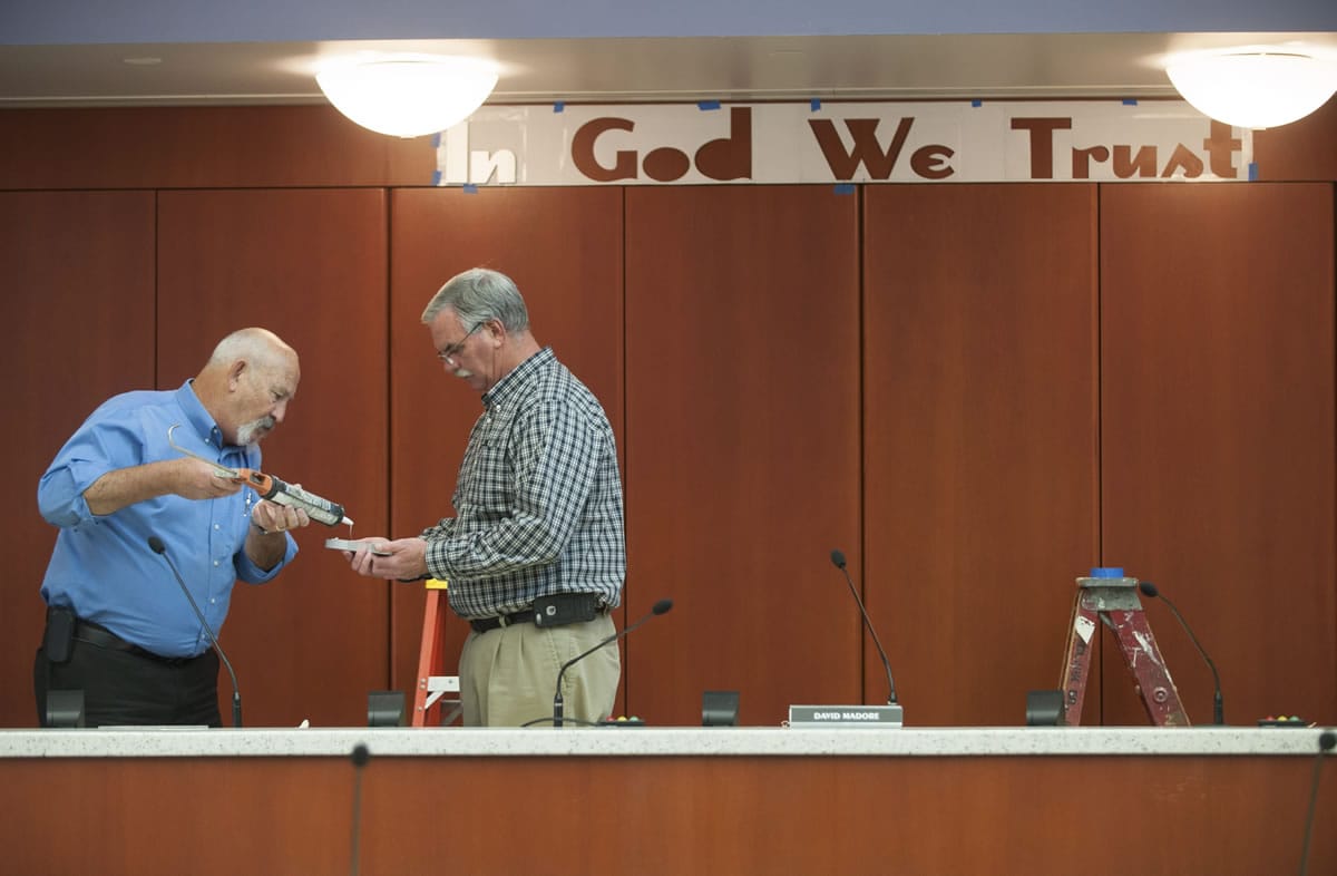County facilities managers Darrel Stump, left and Mike Wright put glue on the back of a letter as the &quot;In God We Trust &quot; slogan is installed Thursday.
