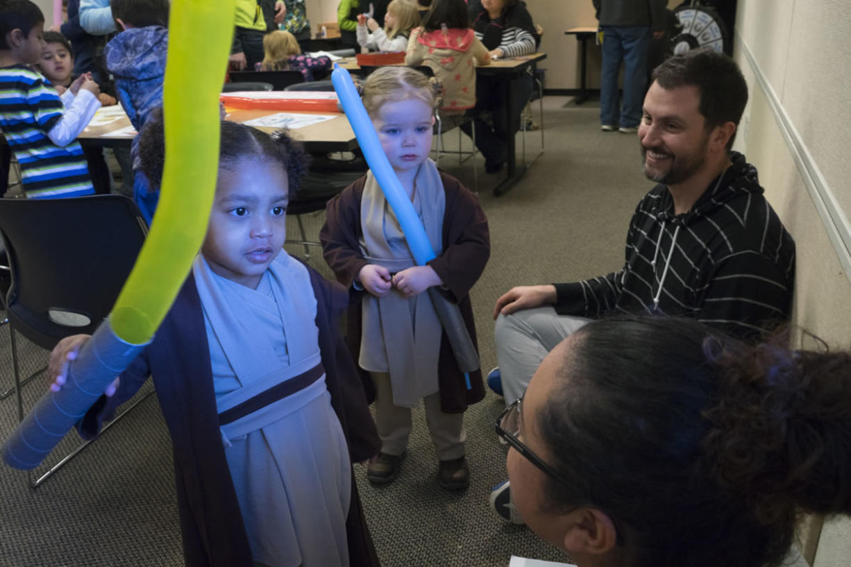 Two-year-olds Chloe Sophia Brent, front left, and Helena Boudreaux, dressed as Jedi knights, play with their light sabers during the &quot;Star Wars&quot; extravaganza at the Camas Public Library on Saturday. Helena&#039;s father, Mathew, back right, is a big &quot;Star Wars&quot; fan and made the costumes for the girls.