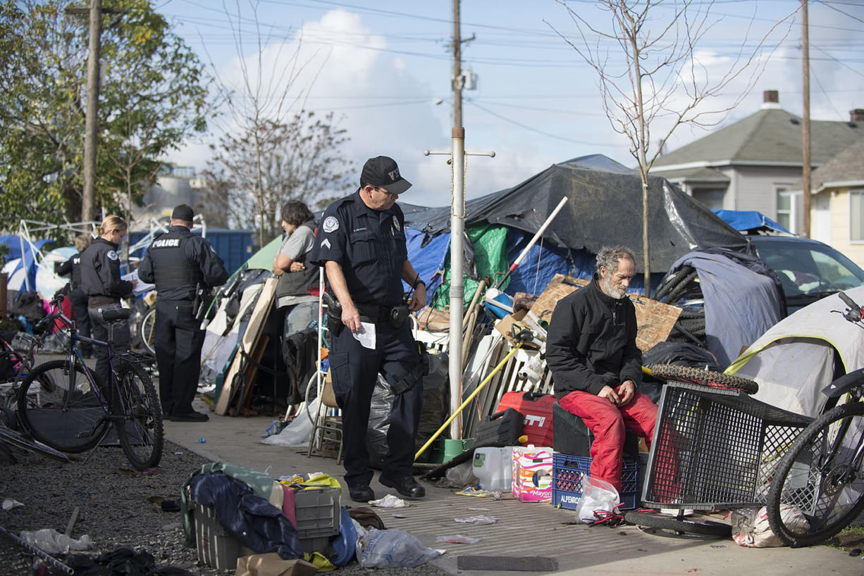 Police Cpl. Stuart Hemstock, center, and other officers work with homeless people Monday morning as they seek to enforce the city's camping law.