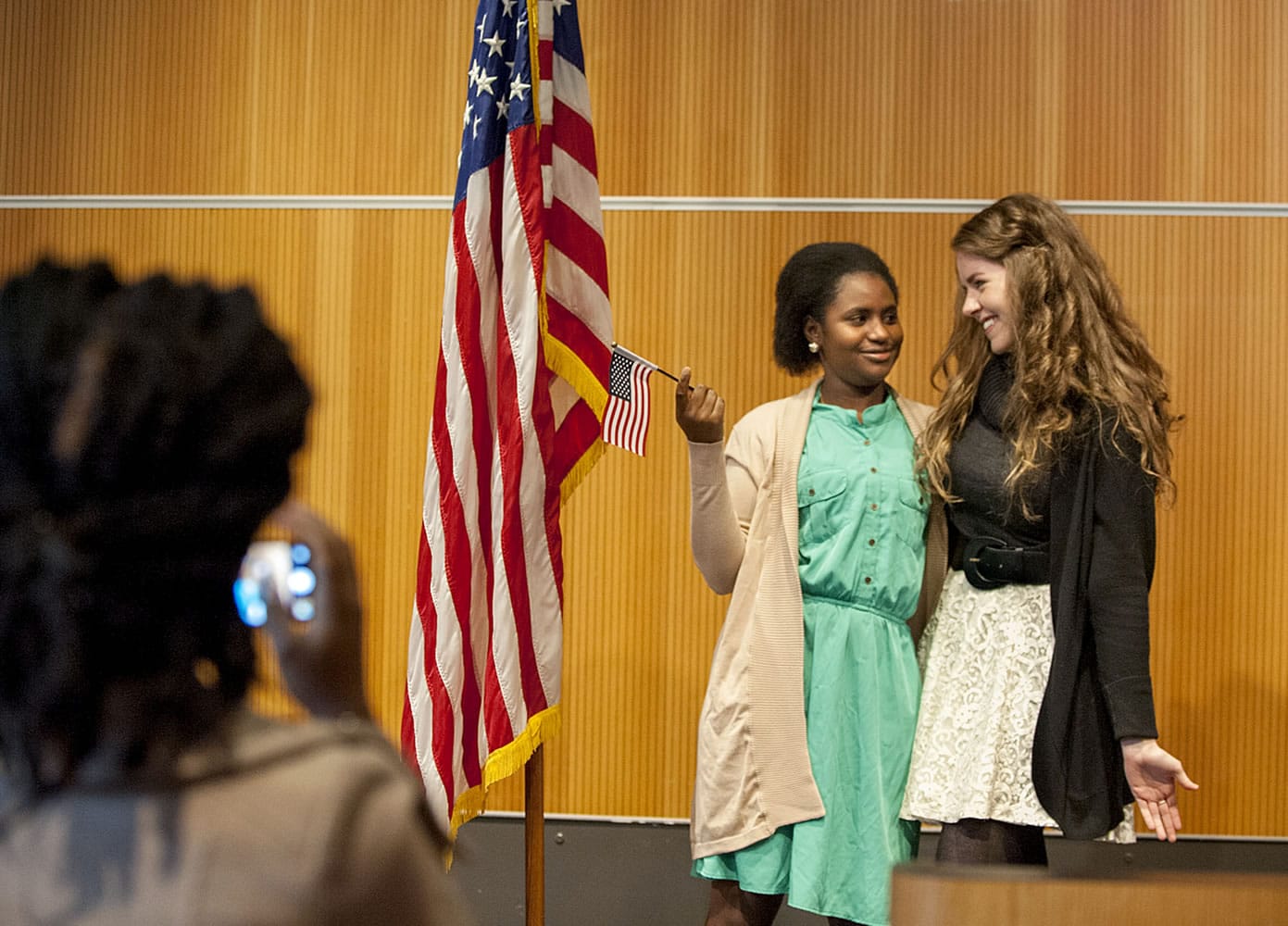 Amina Idy of Portland, holding flag, celebrates her U.S. citizenship Tuesday by having her photograph taken with friend Megan Tragethon at the Vancouver Community Library.
