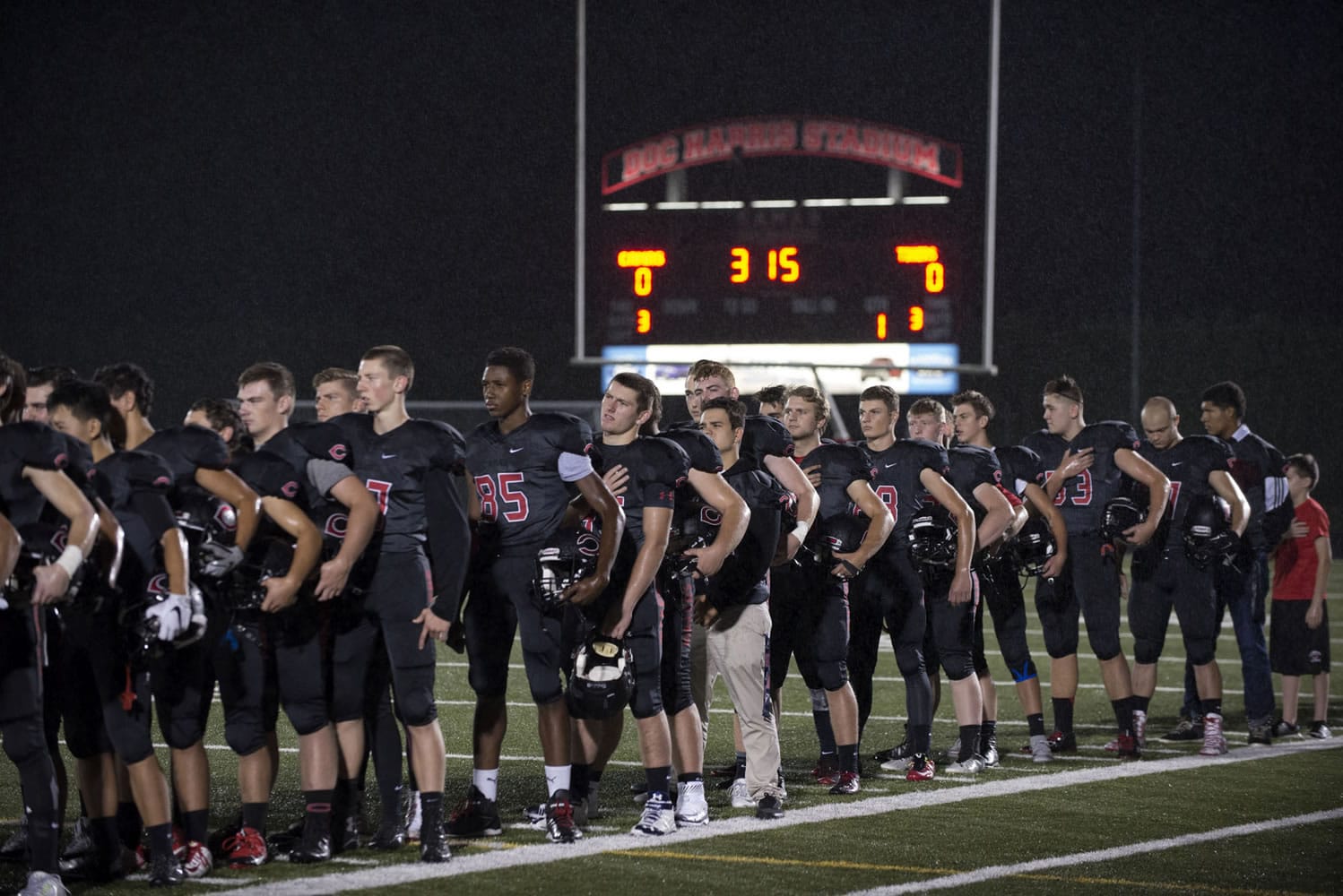 Members of the Camas High School football team remove their helmets as the National Anthem is played Friday night, Oct. 9, 2015 at Doc Harris Stadium.