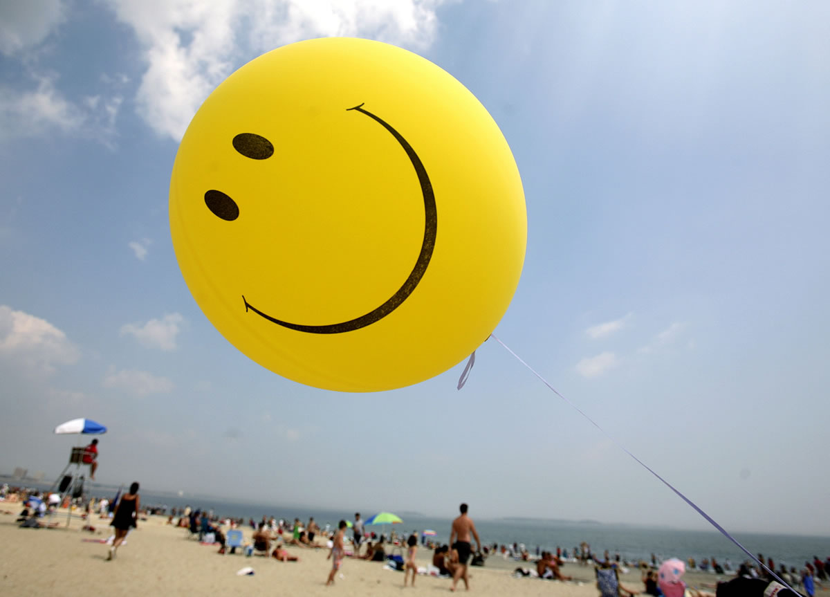 A smiley-face balloon floats over Revere Beach in Revere, Mass., as beachgoers head for the water.